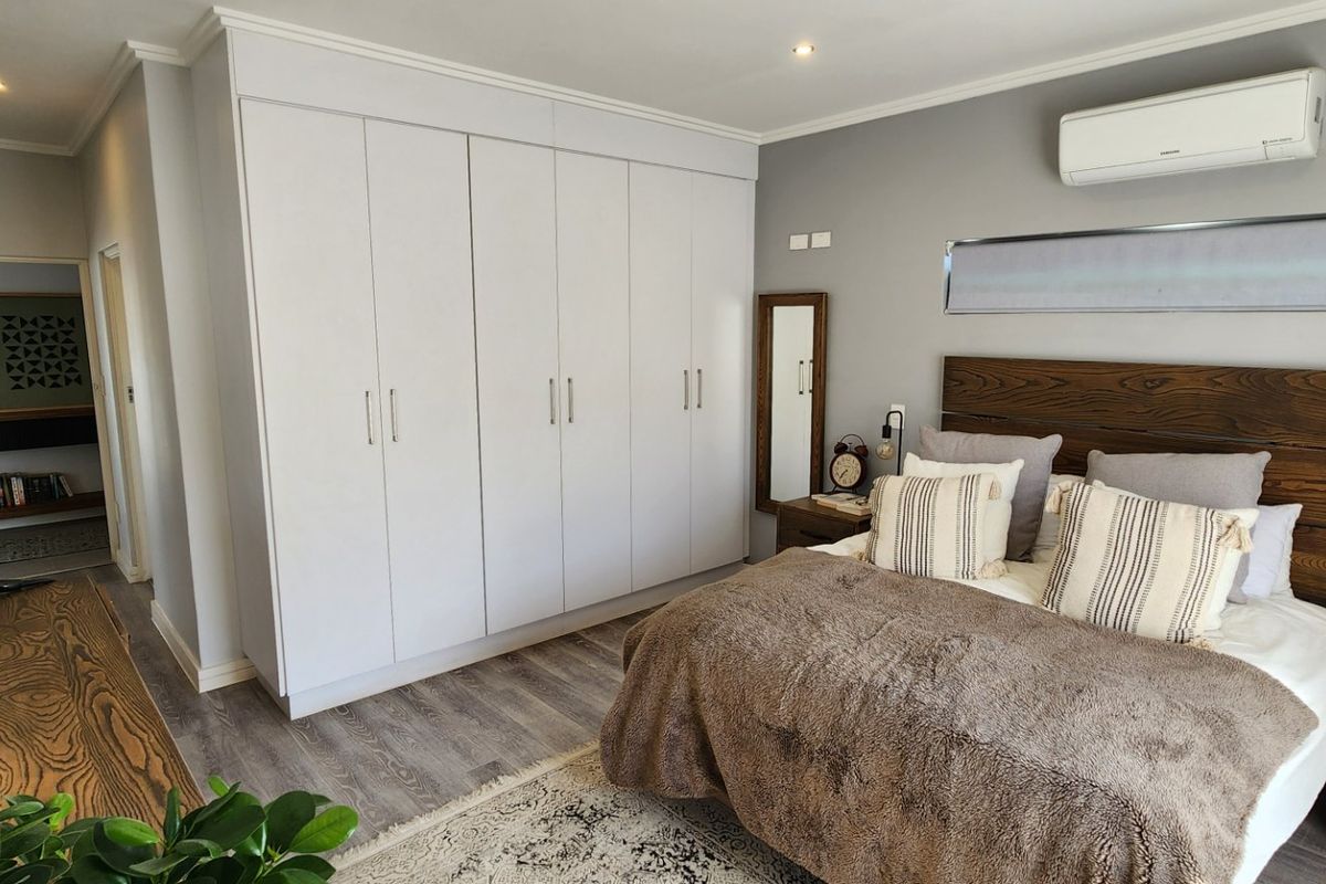 A well-maintained bedroom featuring extensive built-in cupboards, modern laminate flooring, and a wall-mounted air conditioning unit.