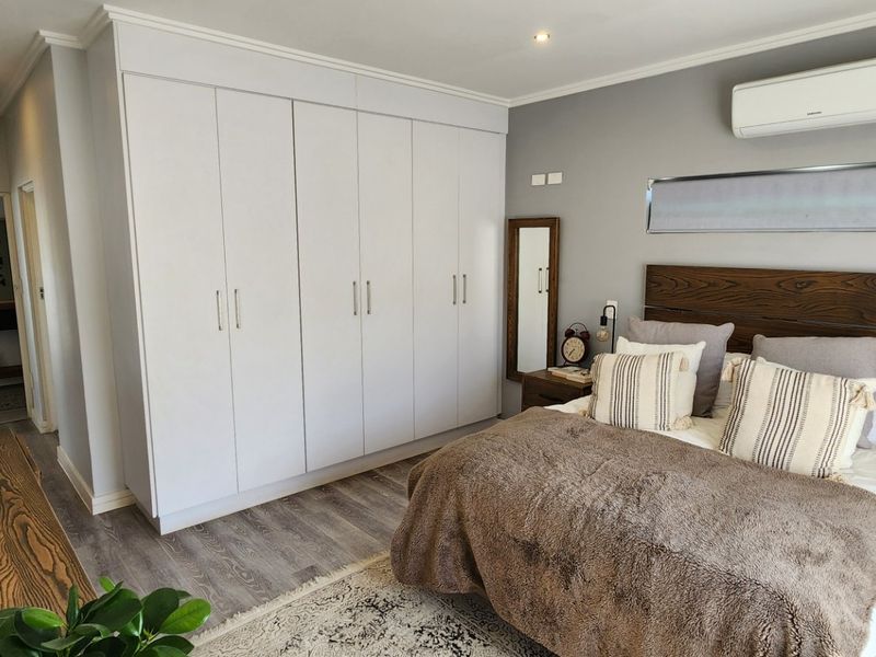 A well-maintained bedroom featuring extensive built-in cupboards, modern laminate flooring, and a wall-mounted air conditioning unit.