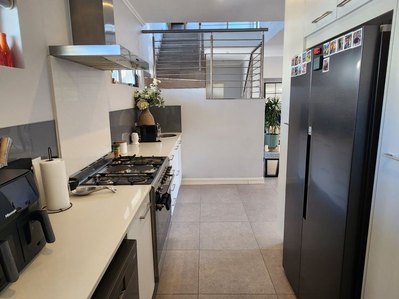 Modern kitchen featuring stone countertops, gas hob, extractor fan, and tiled flooring, with an open-plan layout leading to a staircase.