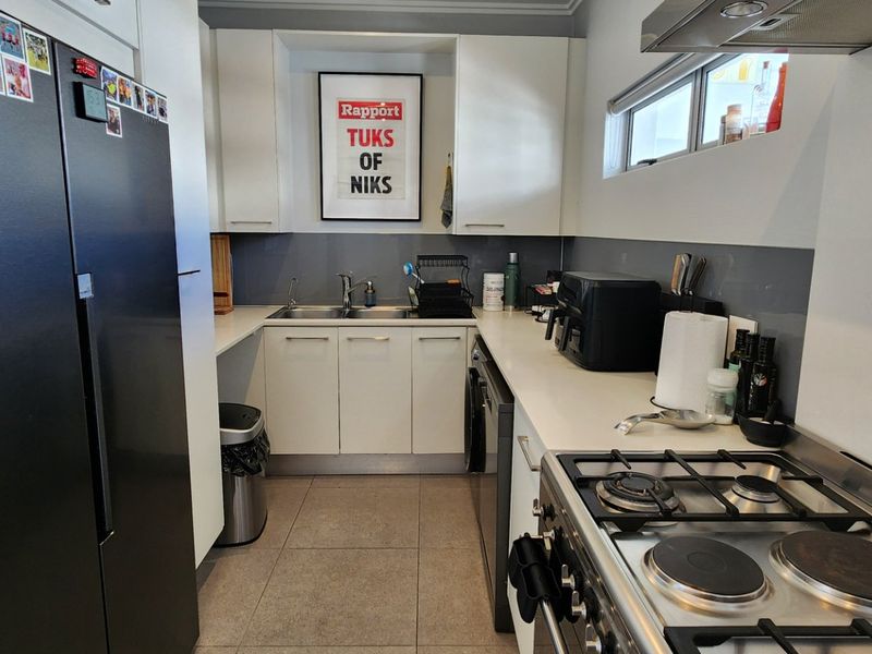 A functional galley-style kitchen featuring white cabinetry, a glass splashback, tiled flooring, and a built-in gas hob with an overhead extractor fan.