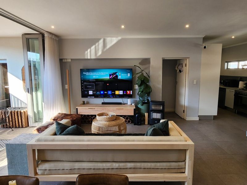 Spacious open-plan living area featuring tiled floors, recessed lighting, and seamless flow to an adjoining balcony, with an integrated kitchen and staircase.