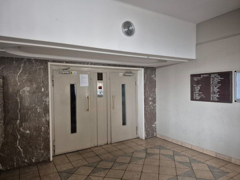 A communal apartment building entrance lobby featuring elevator access, marble wall accents, and a building directory board.