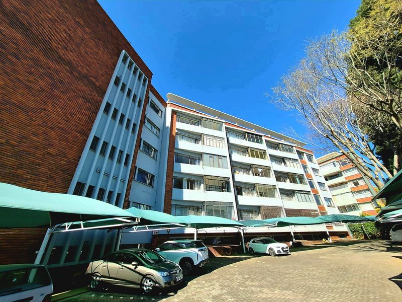 Exterior view of a multi-story apartment building featuring brick and concrete facade, private balconies, and covered parking facilities.