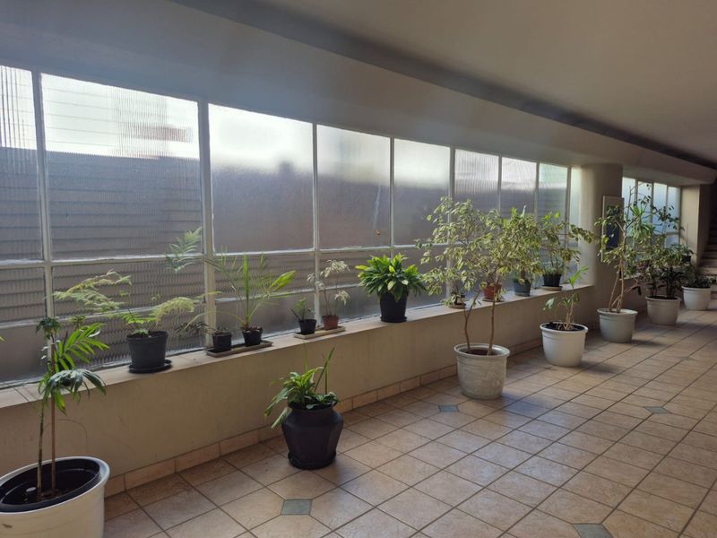A spacious, tiled hallway featuring large window panels and a built-in concrete ledge, providing a bright and functional transition space.