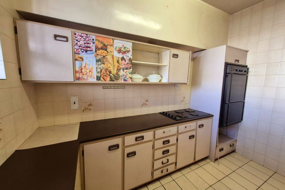 A dated kitchen featuring original built-in cabinetry, an integrated oven and hob, tiled splashbacks, and tiled flooring, offering potential for a modern renovation.