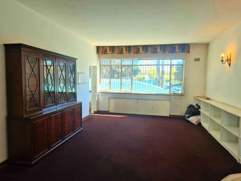 Spacious living area featuring built-in shelving, large windows with security bars, and wall-to-wall carpeting, offering a blank canvas for renovation.