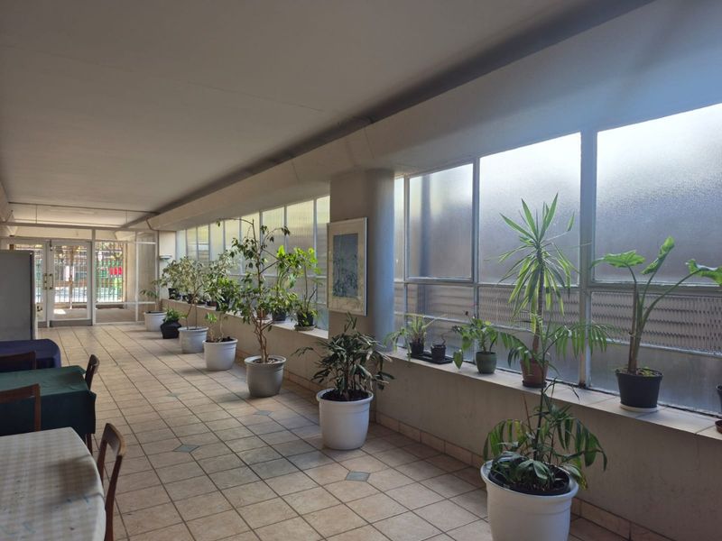 A spacious, covered balcony or sunroom featuring tiled flooring and extensive glass windows, providing a bright and airy transition space.