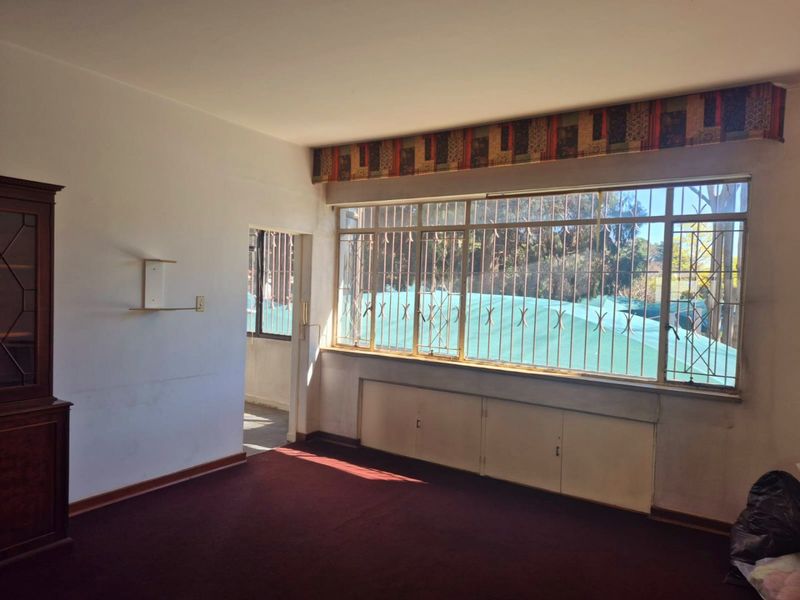 A spacious living area featuring built-in cabinetry, large windows with security bars, and carpeted flooring, offering a blank canvas for renovation.