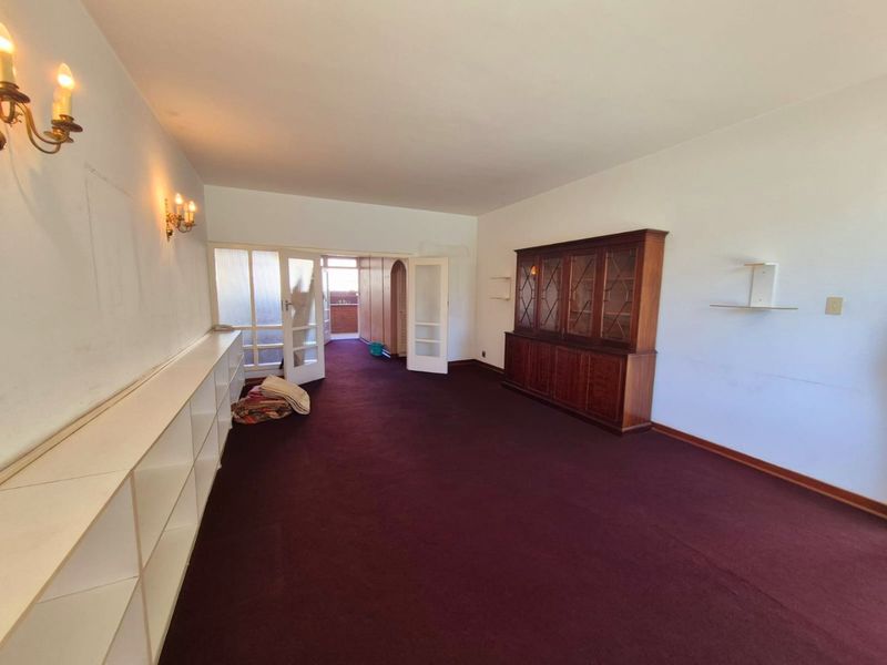 Spacious living area featuring built-in shelving, wall-mounted lighting, and direct access to an adjoining room through glass-paneled doors.