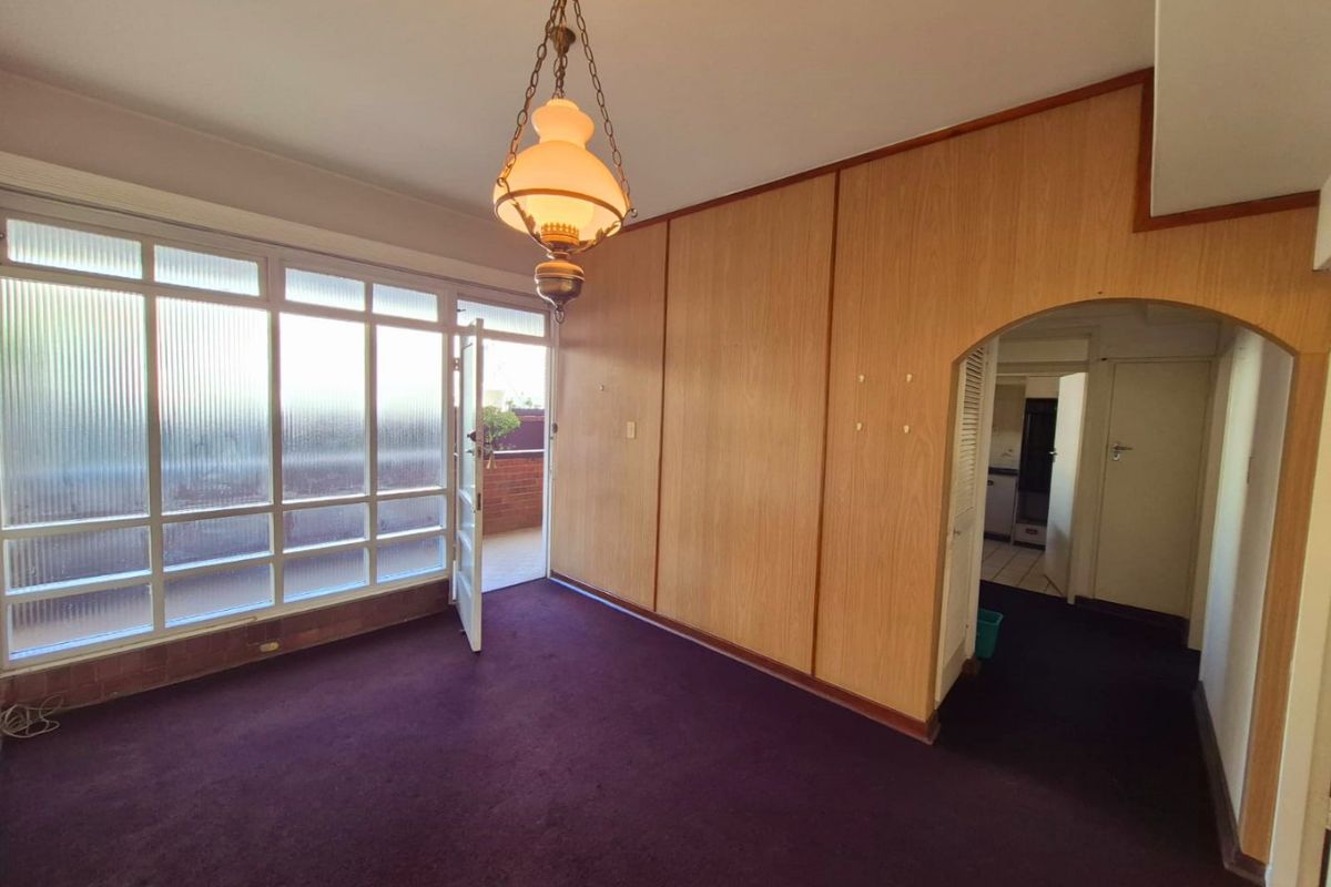 An empty living room featuring wood paneling, a classic pendant light, and large windows leading to an outdoor balcony area.