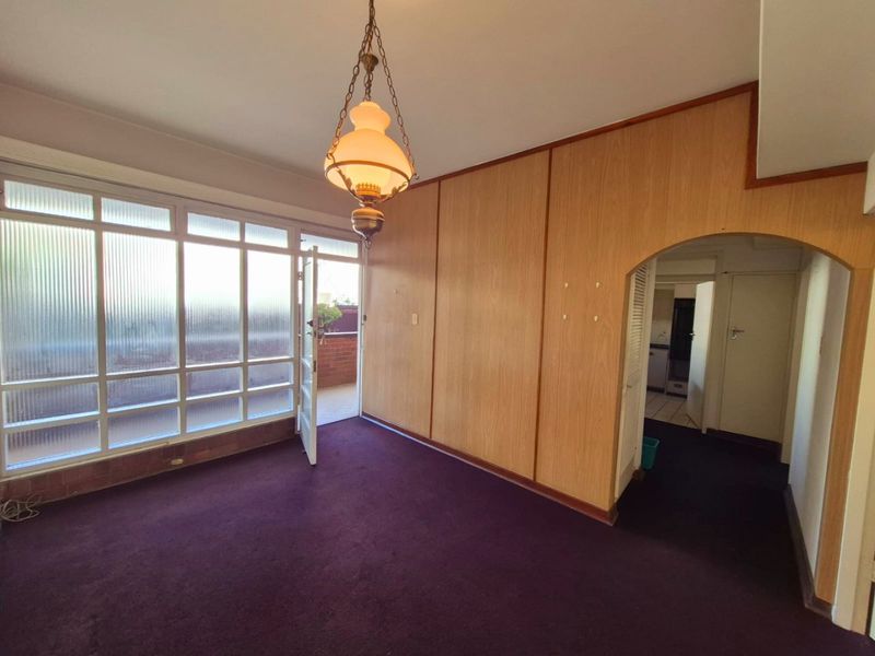 An empty living room featuring wood paneling, a classic pendant light, and large windows leading to an outdoor balcony area.