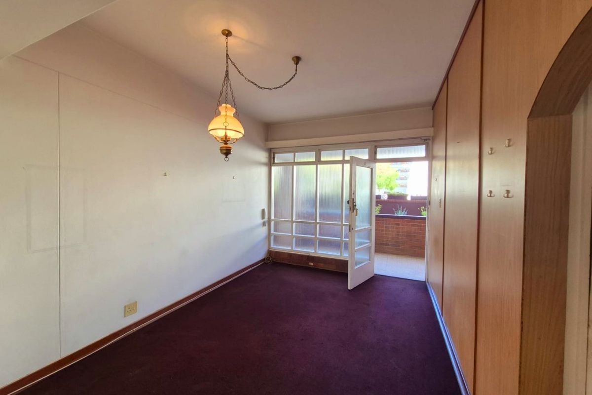 An empty bedroom featuring built-in wooden cupboards, carpet flooring, and a glass-paneled door providing access to an outdoor balcony area.