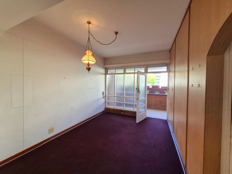 An empty bedroom featuring built-in wooden cupboards, carpet flooring, and a glass-paneled door providing access to an outdoor balcony area.