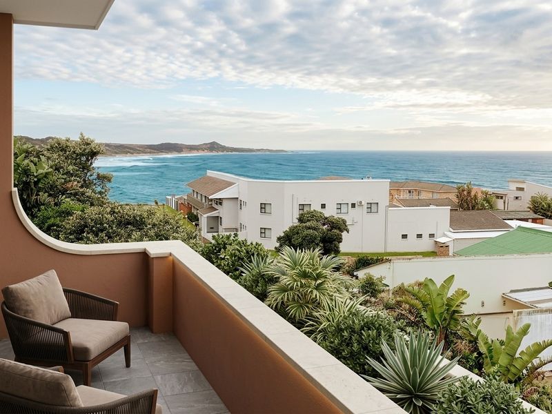 A well-maintained balcony featuring tiled flooring and a stone-capped parapet wall, offering expansive views of the coastline and surrounding neighborhood.
