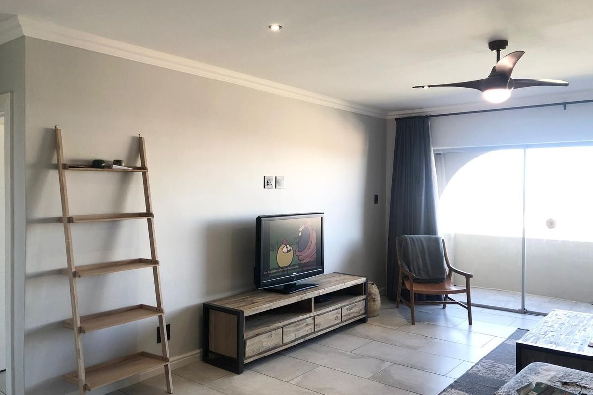 A well-lit living room featuring tiled flooring, a modern ceiling fan, and a large sliding glass door providing access to an outdoor area.