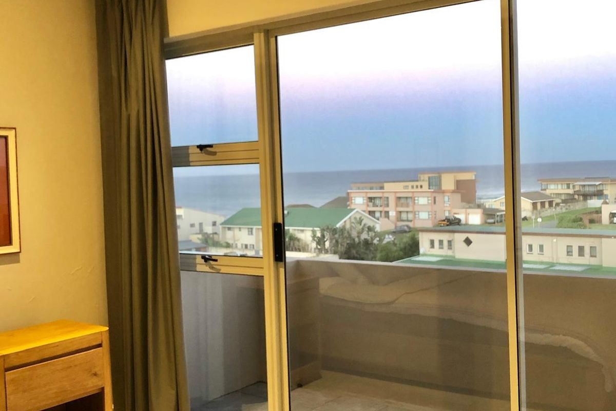 A bedroom featuring large sliding glass doors that provide access to a balcony and offer scenic coastal views.