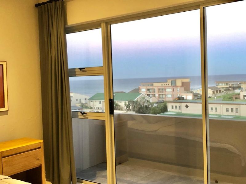 A bedroom featuring large sliding glass doors that provide access to a balcony and offer scenic coastal views.