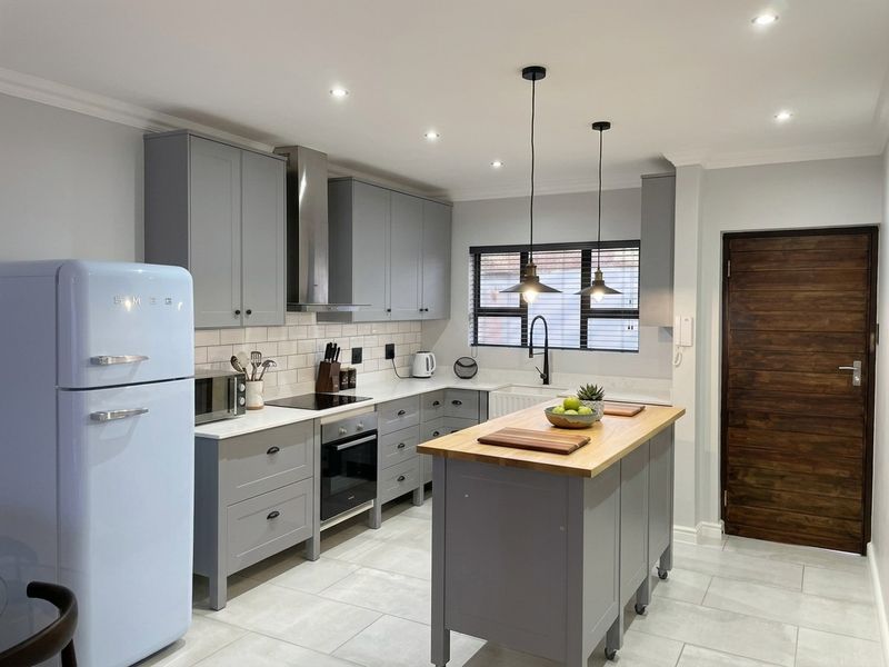 Modern kitchen featuring grey cabinetry, stone countertops, a central island, subway tile backsplash, and high-quality integrated appliances with recessed and pendant lighting.