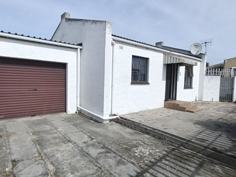 Front exterior view of a single-story house featuring a garage with a roller shutter door, a paved driveway, and a small tiled entrance patio.