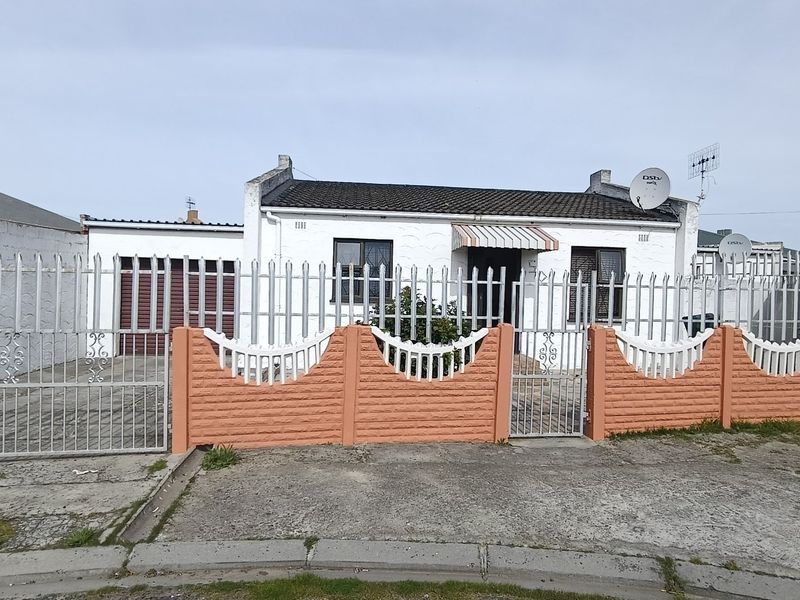 Front elevation of a single-story house featuring a tiled roof, secure metal fencing, a precast boundary wall, and a paved driveway with garage access.