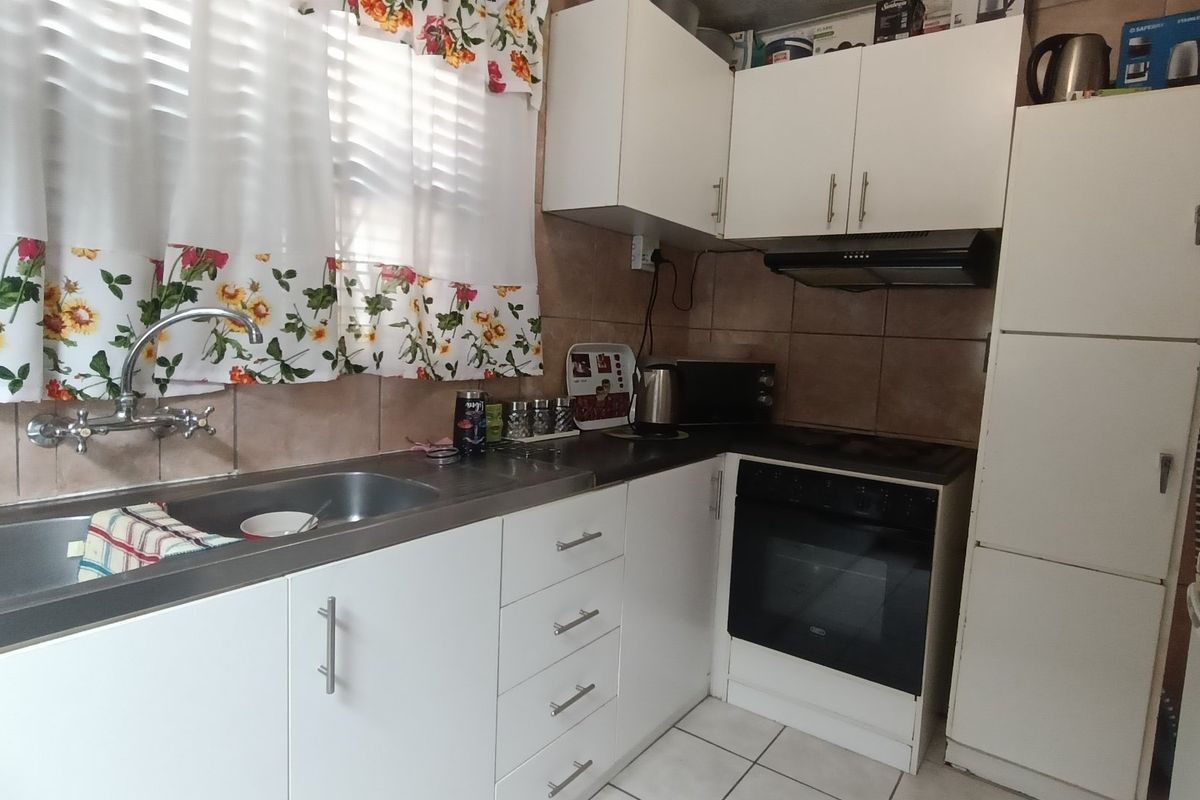A functional kitchen featuring white cabinetry, a stainless steel sink, built-in oven with hob, extractor fan, and tiled backsplash.