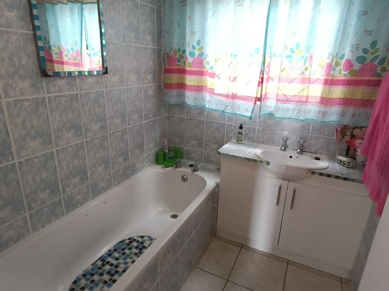 A functional bathroom featuring a built-in bathtub, a vanity cabinet with a ceramic basin, and full-height wall tiling.