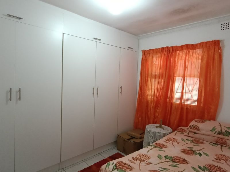 A bedroom featuring extensive white built-in cupboards and a ceiling vent, providing functional storage space.