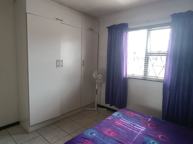 A functional bedroom featuring built-in cupboards, tiled flooring, and a window fitted with security bars.