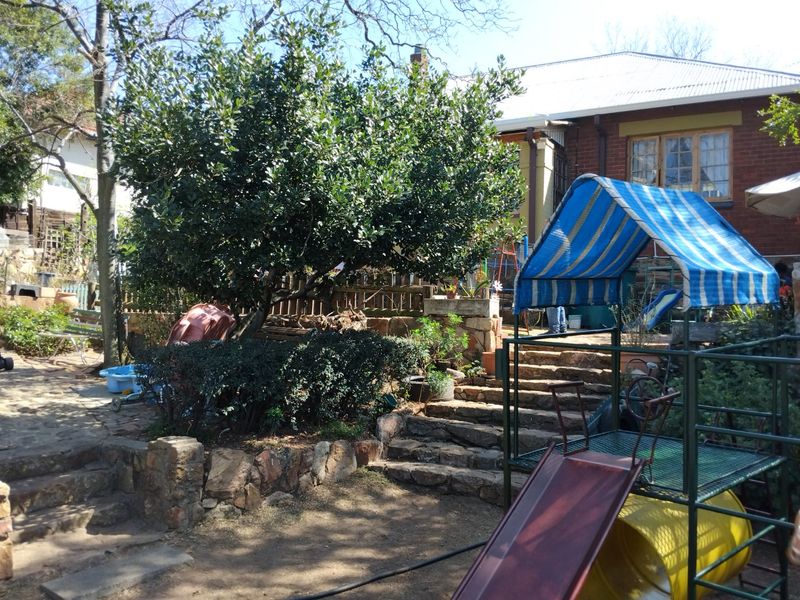 Rear garden area featuring stone retaining walls, stone stairs, and a brick building facade with a corrugated metal roof.