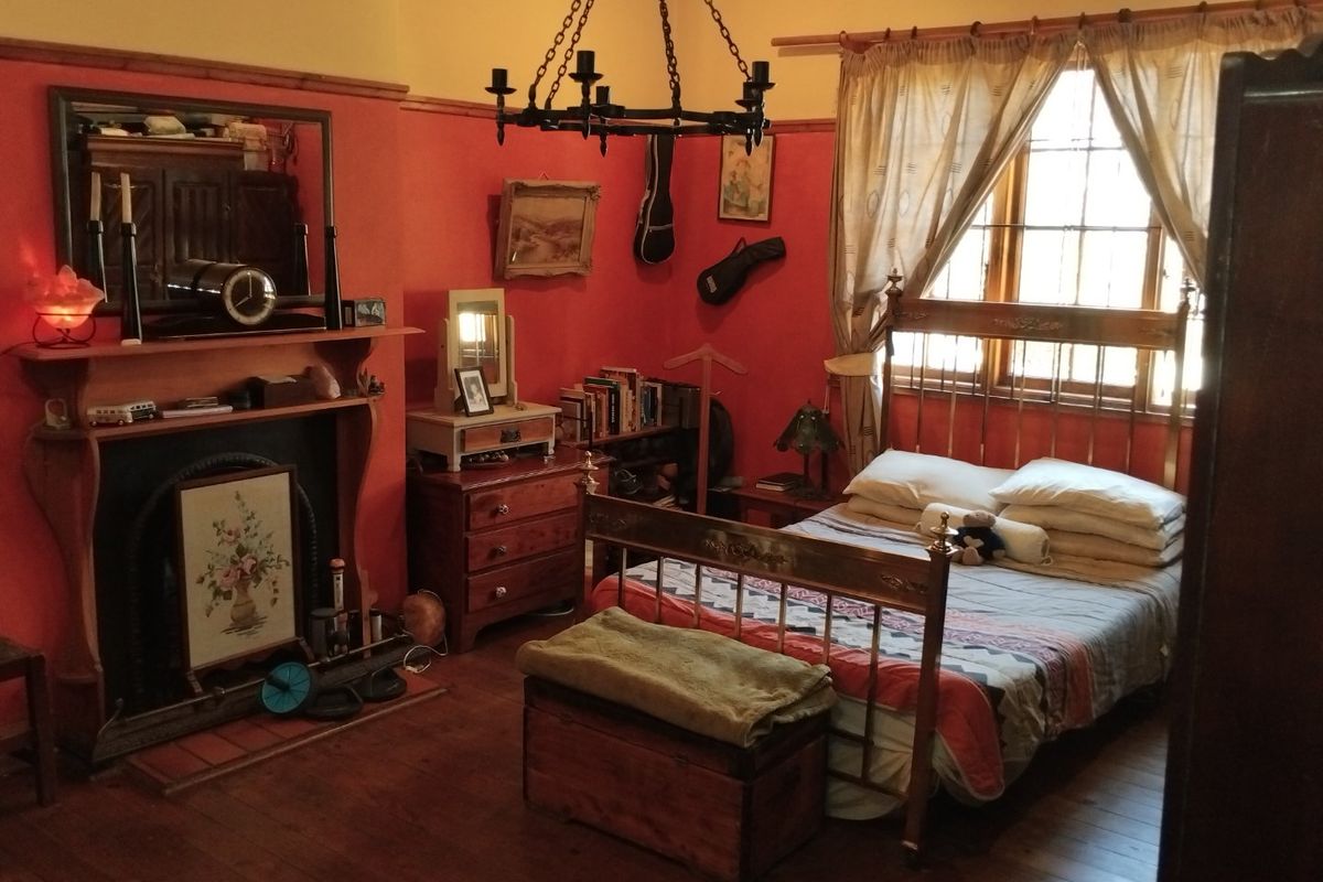A bedroom featuring a traditional fireplace, timber flooring, and a wrought iron chandelier, offering a classic and cozy atmosphere.