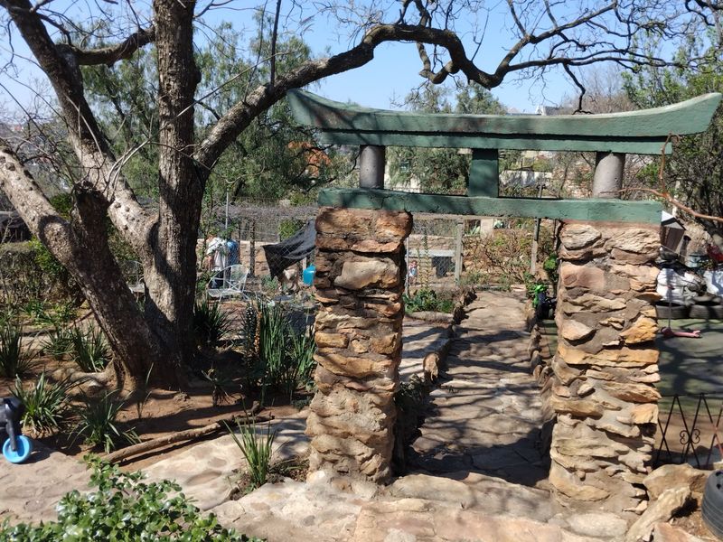 A garden area featuring a stone pathway leading through a decorative stone and timber gate structure surrounded by mature trees.