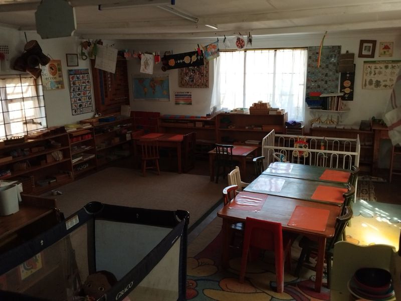 A multi-purpose room currently utilized as a classroom or play area, featuring built-in shelving units and natural light from large windows.
