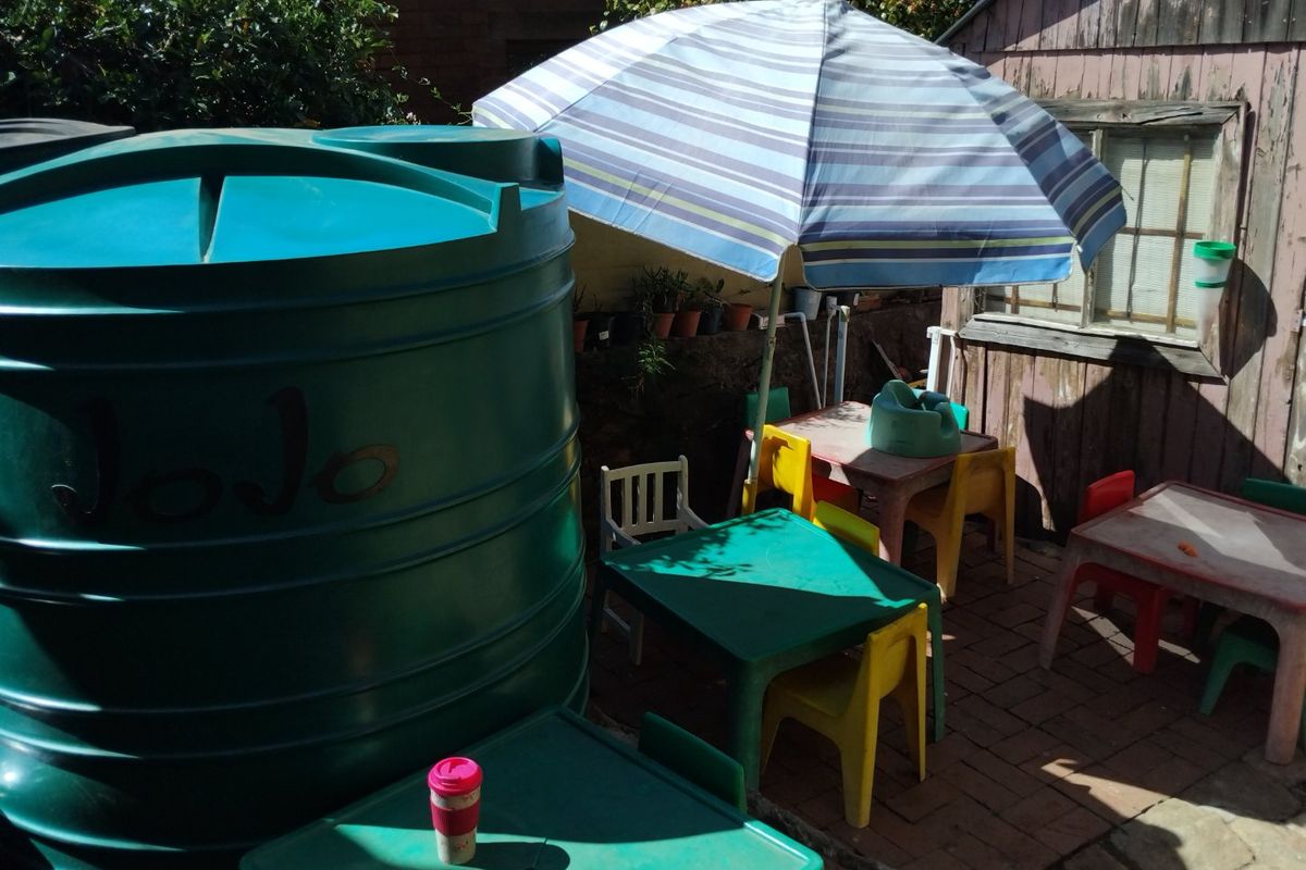 Rear outdoor area featuring a large water storage tank, paved patio space, and a weathered timber shed structure.