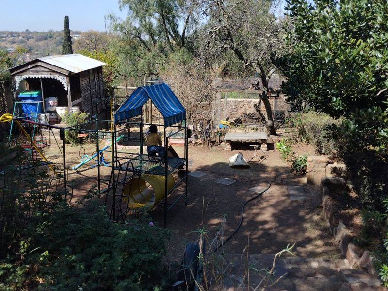 A backyard garden area featuring a wooden storage shed, stone retaining walls, and established trees, offering potential for landscaping and outdoor improvement.