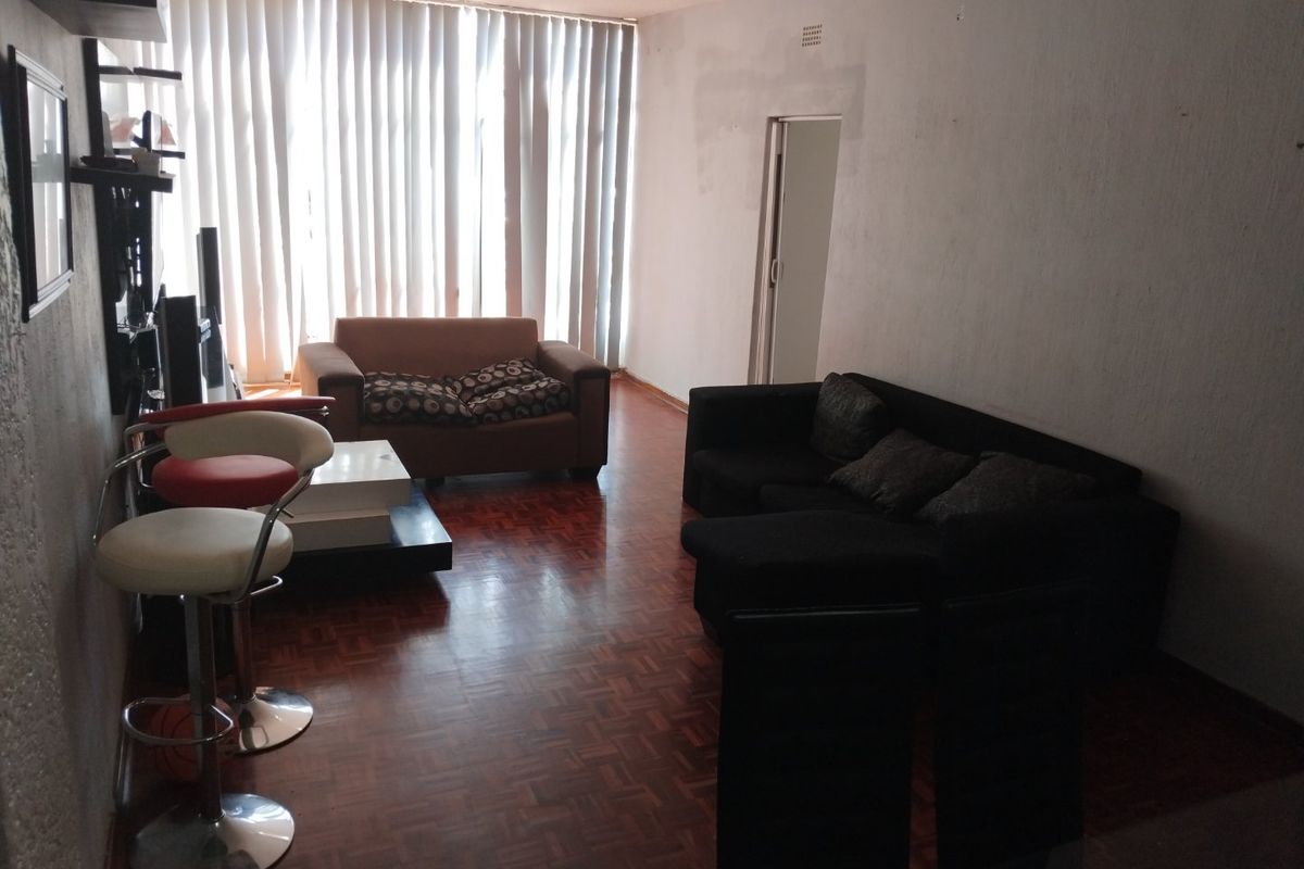 A living room featuring traditional parquet flooring, vertical window blinds, and ceiling track lighting, requiring cosmetic updates to the wall finishes.