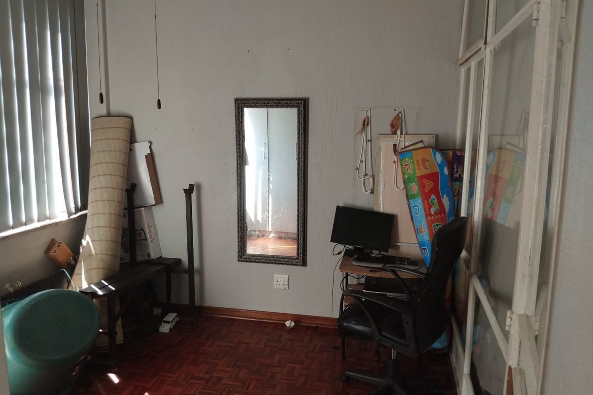 A bedroom featuring parquet flooring and vertical blinds, currently used as a storage and workspace area.