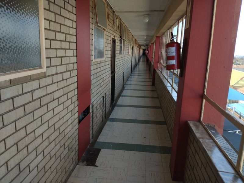 A long, open-air apartment building hallway featuring brick walls, tiled flooring, and safety equipment, showing signs of wear and age.