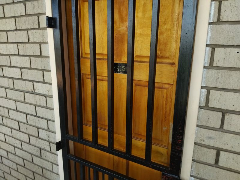 Apartment entrance featuring a timber door protected by a black metal security gate set against a brick exterior wall.