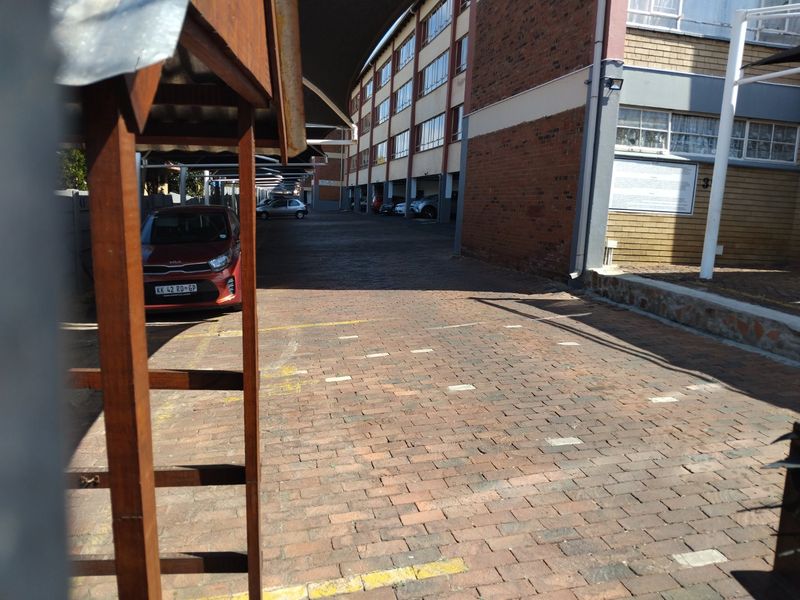 Exterior view of the apartment complex featuring a paved driveway and covered parking bays alongside the brick building facade.
