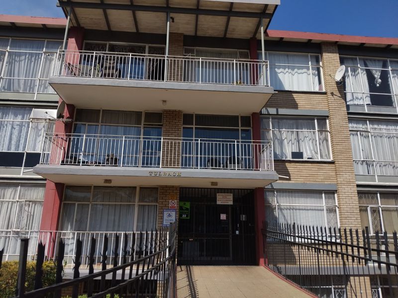Front elevation of the Tulbach apartment building featuring brick facade, multiple balconies with metal railings, and a secure gated entrance with ramp access.