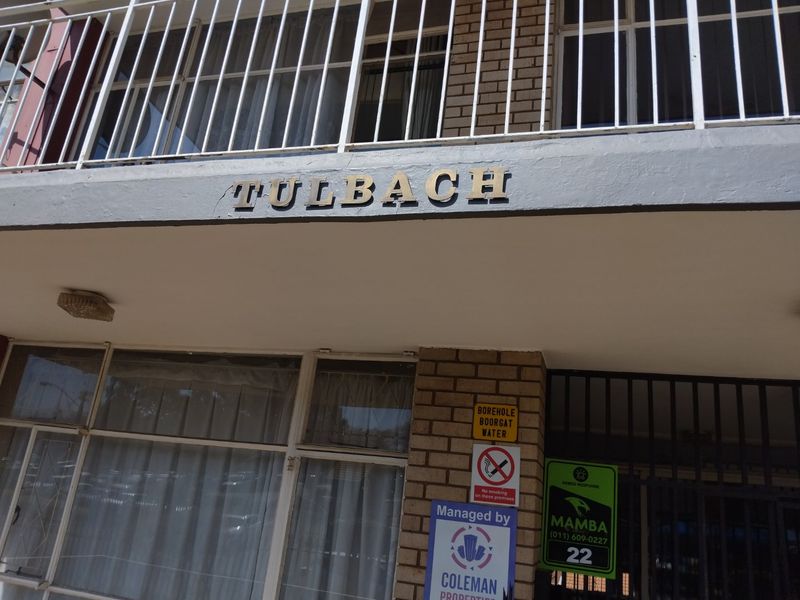 Front entrance view of the Tulbach apartment building, featuring brick facade, security gate, and balcony railing.