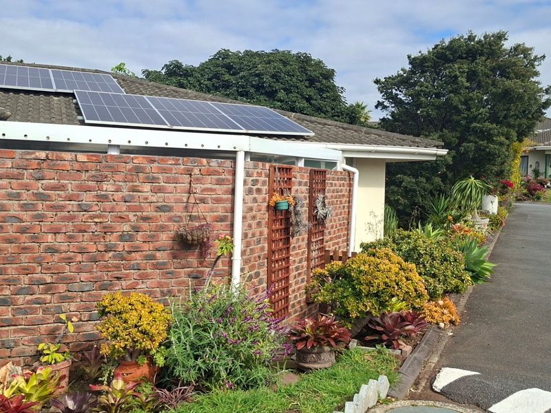 Front exterior view of the property featuring a face brick wall, tiled roof with installed solar panels, and a paved driveway.
