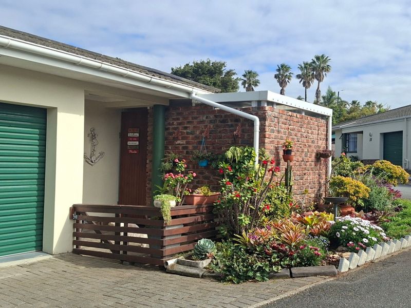 Front elevation of the property featuring a green roller garage door, brickwork detailing, and a well-maintained garden bed.