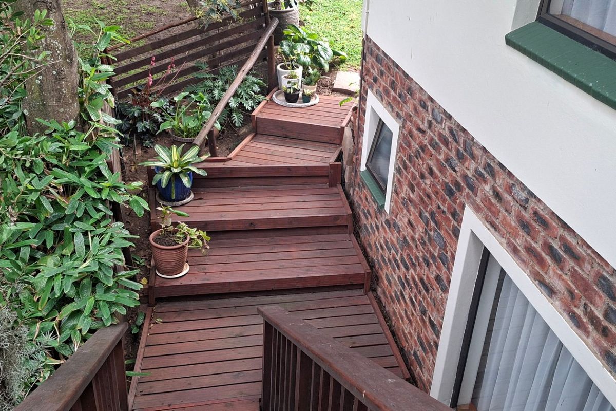 A well-maintained timber staircase and deck area leading to the rear garden, featuring exposed brickwork and established surrounding greenery.