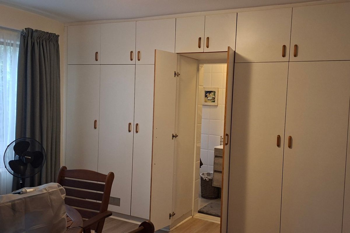Bedroom featuring extensive floor-to-ceiling built-in cupboards and laminate flooring, with direct access to an en-suite bathroom.
