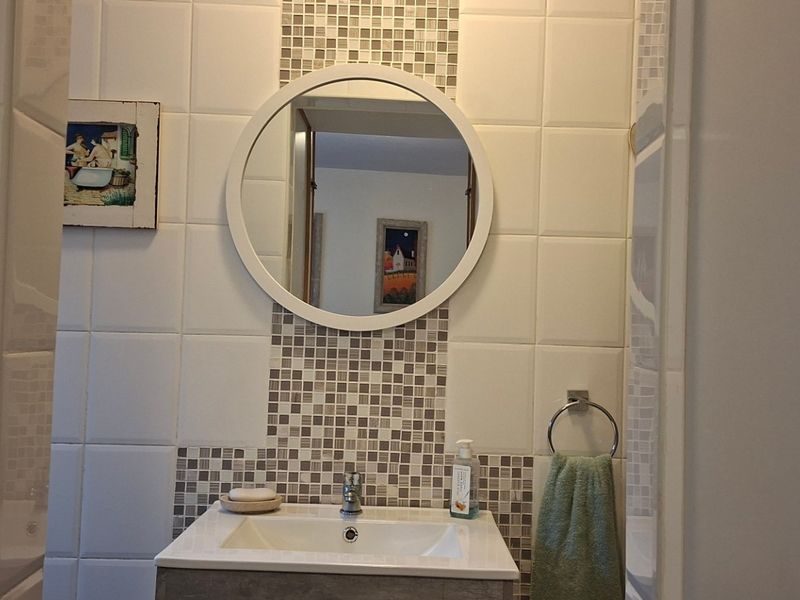 A compact bathroom featuring a modern vanity basin, circular wall mirror, and decorative mosaic tile splashback.