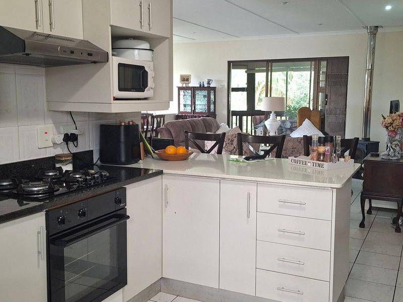 Open-plan kitchen featuring granite countertops, built-in appliances, and tiled flooring, flowing seamlessly into a living area with a wood-burning fireplace and garden access.