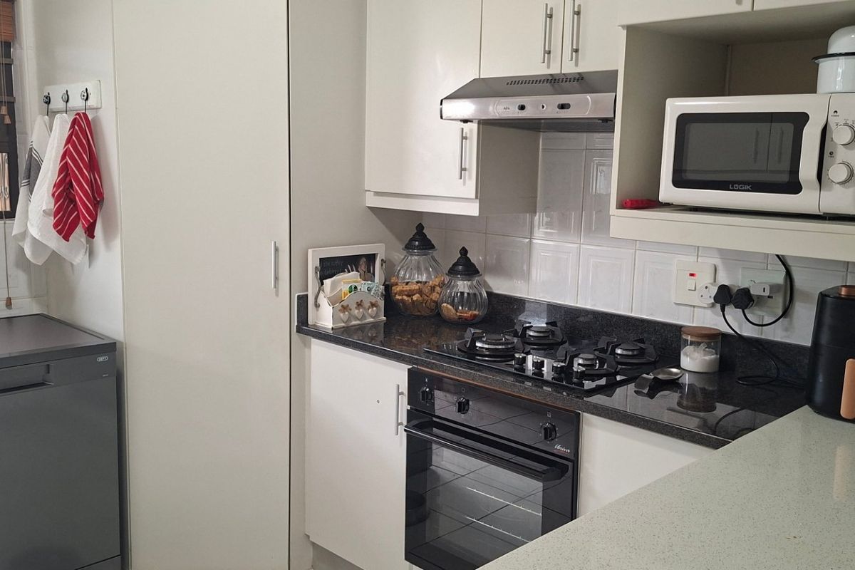 A functional kitchen featuring white cabinetry, granite countertops, a gas hob, built-in oven, and an extractor fan, providing a clean and practical cooking space.
