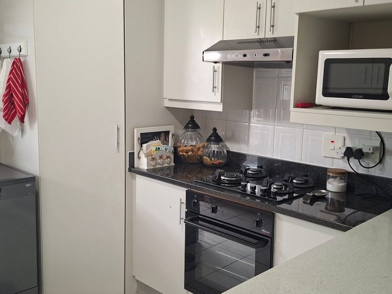 A functional kitchen featuring white cabinetry, granite countertops, a gas hob, built-in oven, and an extractor fan, providing a clean and practical cooking space.