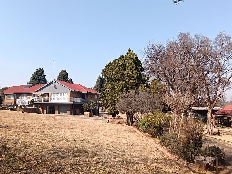 A wide view of the rear of the property featuring a multi-level brick house with a balcony, tiled roof, and surrounding garden area.